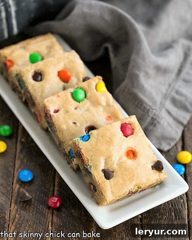 M & M Blondies arranged neatly on a narrow white tray, highlighting their perfect squares and colorful M&Ms.