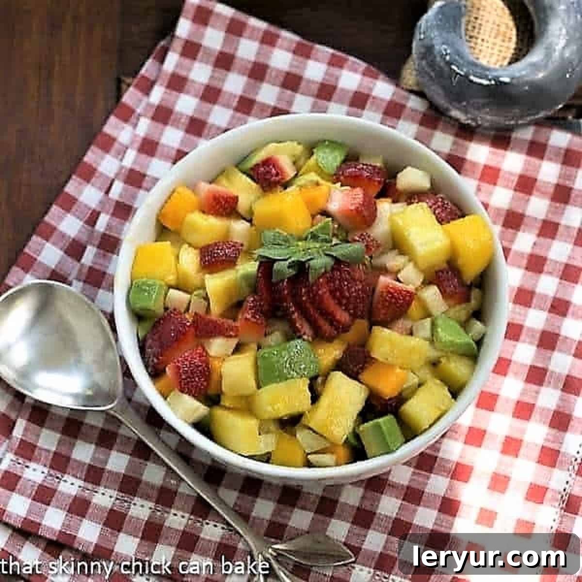A vibrant Mango Strawberry Avocado Salad in a pristine white bowl, resting on a cheerful red and white checkered napkin.