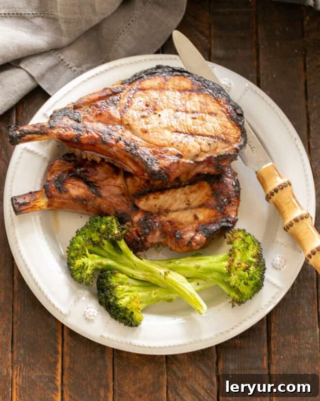 Two perfectly grilled pork chops and a side of steamed broccoli on a pristine white dinner plate, ready to be served.