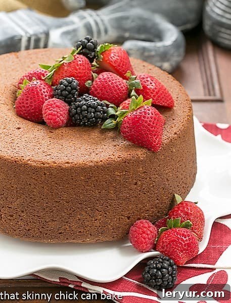 A magnificent whole Vanilla Pound Cake, elegantly presented on a white ruffled platter, generously adorned with a vibrant medley of fresh berries.