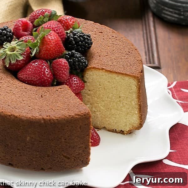 A whole Vanilla Pound Cake on a elegant white platter, with a single slice removed revealing its dense, moist crumb, and the center filled with a bounty of fresh, colorful berries.