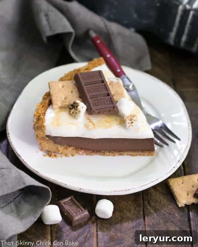 A close-up of a slice of S'mores Pie on a white dessert plate, accompanied by a red-handled fork. The layers are clearly visible and the marshmallow topping is beautifully toasted.