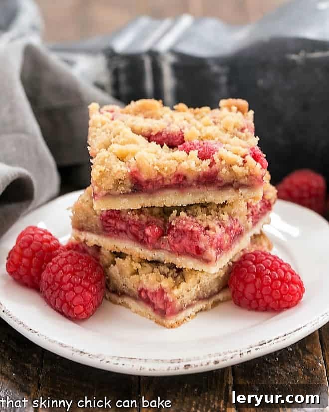 Streusel Topped Raspberry Squares stacked on a small plate with fresh raspberries. Close-up view of the layers.