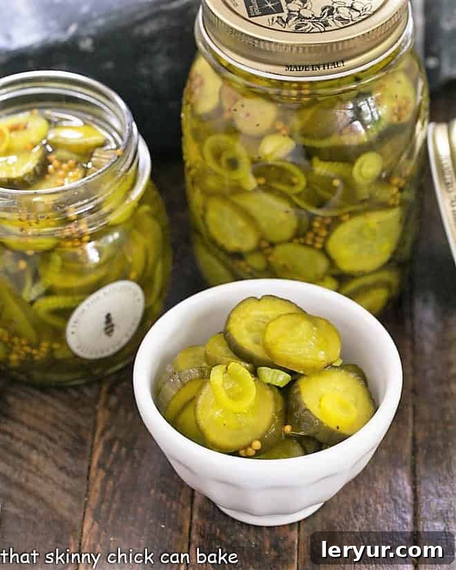 Two jars of Easy Bread and Butter Pickles plus a white bowl filled with pickle slices, ready for serving.