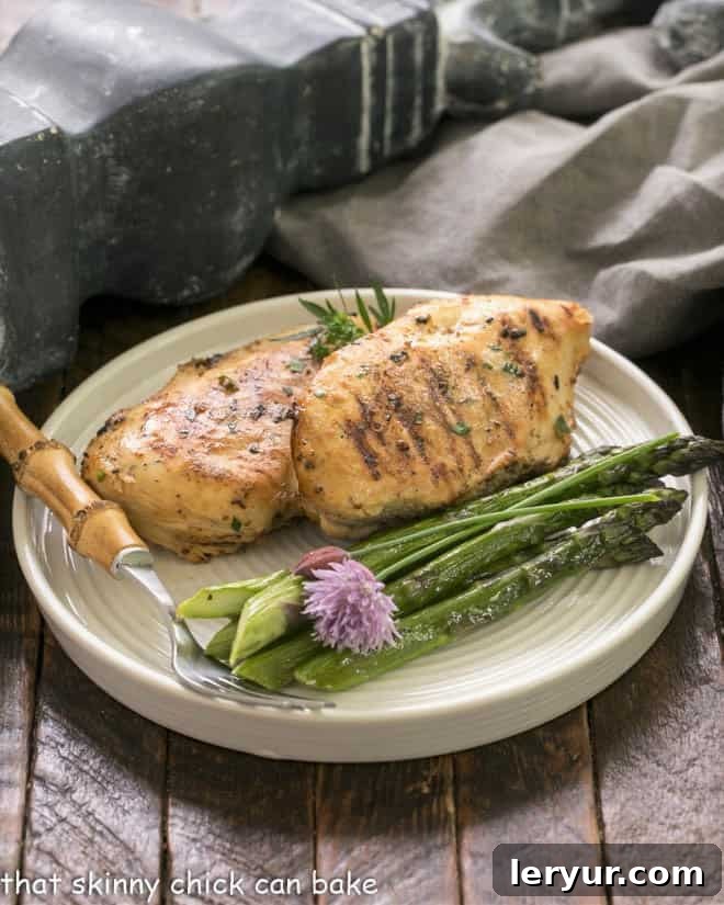 Zesty Mustard Lime Chicken 5 Two perfectly grilled chicken breasts on a pristine white dinner plate, garnished with vibrant asparagus spears and a bamboo-handled fork.