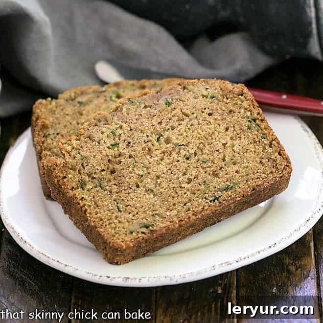 Two slices of zucchini bread on a round white plate with a red handle knife