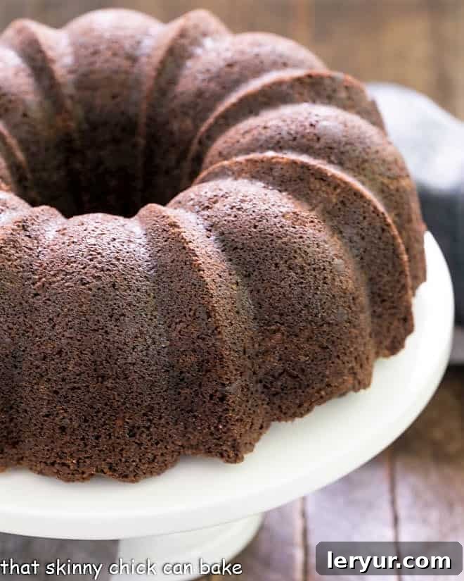 Chocolate Zucchini Bundt Cake on a white cake plate, generously drizzled with chocolate glaze.
