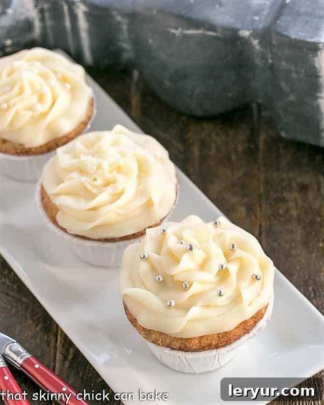 A trio of delicious vanilla cupcakes with thick cream cheese frosting presented on a rustic white rectangular tray.
