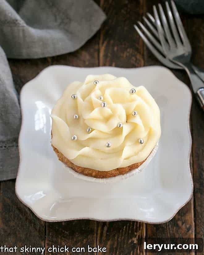 Overhead view of an Easy Vanilla Cupcake on a white plate with a sprig of mint and a small spoon.