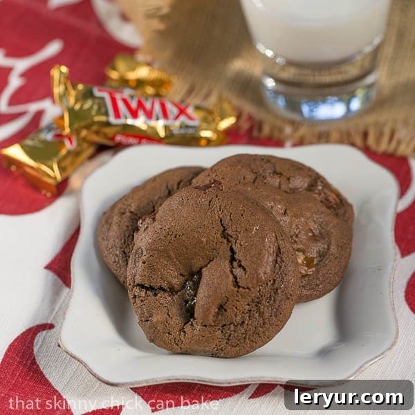 Double Chocolate Twix Cookies - rich, chocolate cookies filled with chunks of decadent Twix bars! Three Double Chocolate Twix Cookies on a square white plate, showcasing their rich color and inviting texture.