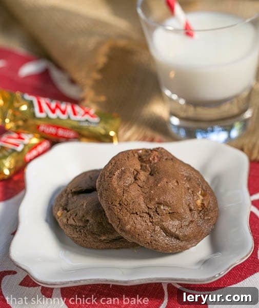 Double Chocolate Twix Cookies - rich, chocolate cookies filled with chunks of decadent Twix bars! Two Double Chocolate Twix Cookies on a white plate next to a refreshing glass of milk, inviting a delicious break.