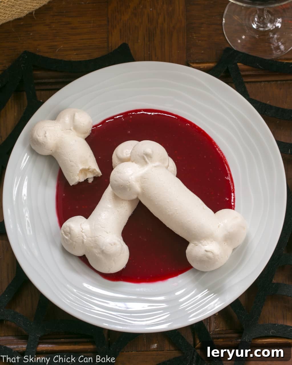 Crisp Meringue Bones dramatically broken over a vivid raspberry sauce on a white plate, perfect for a spooky Halloween dessert.