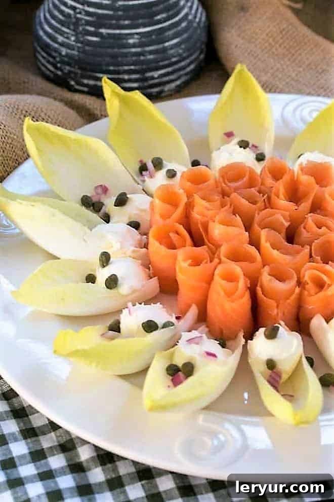 Smoked salmon roses artfully arranged on a round white serving plate with crisp endive, creamy creme fraiche, briny capers, and finely minced red onion.