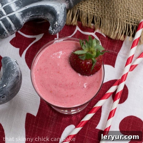 Overhead view of a vibrant berry smoothie with two red and white striped straws, garnished with fresh berries.