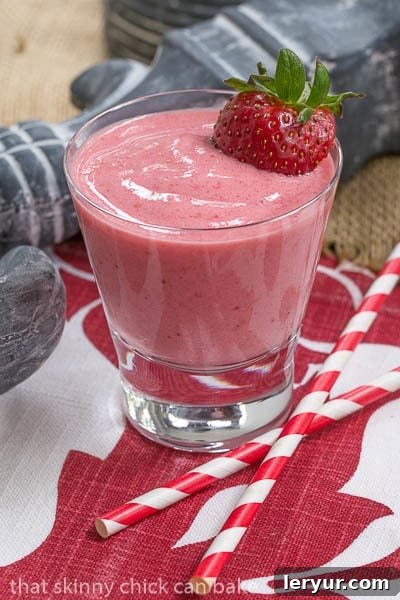A refreshing berry smoothie in a clear glass, garnished with fresh berries and a straw, on a rustic wooden surface.