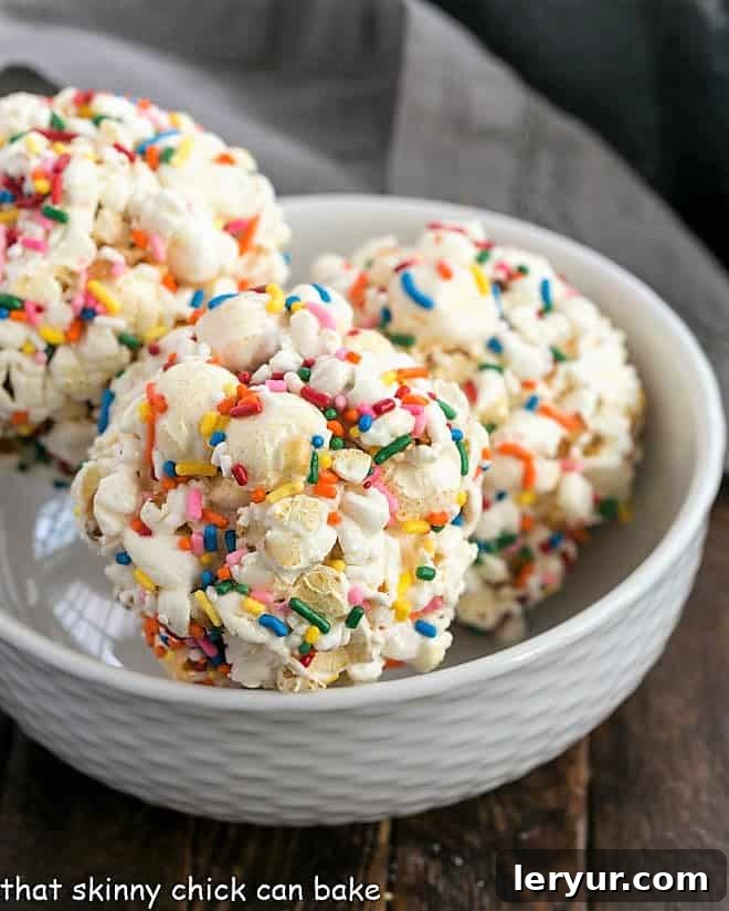 Popcorn Balls Recipe - A simple popcorn treat that's great for all ages! Three Easy Marshmallow Popcorn Balls in a rustic white bowl, showcasing their inviting texture.