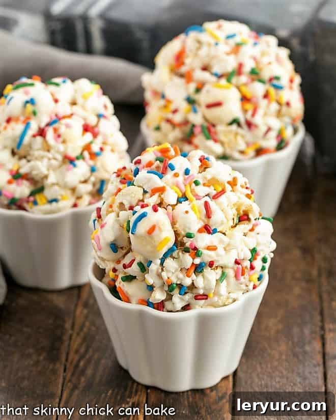 Popcorn Balls Recipe with marshmallows - A simple popcorn treat that's great for all ages! Three Marshmallow Popcorn Balls in scalloped white ramekins, ready to be enjoyed.