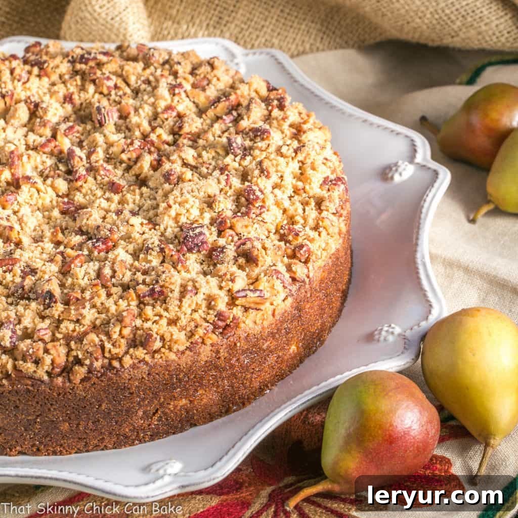 Pear Streusel Coffee Cake - A moist, tender, crumb topped coffee cake that's perfect for company! A stunning Pear Streusel Coffee Cake, whole and beautifully golden-brown, displayed on an elegant white platter, surrounded by glistening fresh pears.