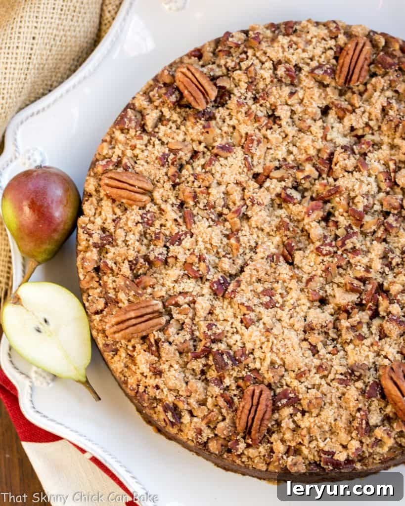 Pear Streusel Coffee Cake - A moist, tender, crumb topped coffee cake that's perfect for company! An inviting overhead shot of the entire Pear Streusel Coffee Cake, rich with golden streusel and a hint of pear, resting on a pristine white serving dish, adorned with miniature fresh pears.