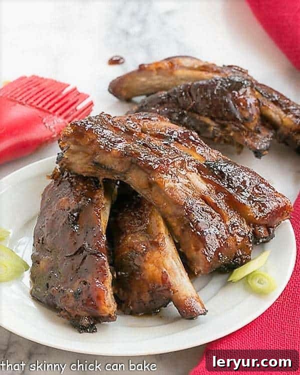 Asian Baby Back Ribs - Finger licking good with a seriously delicious glaze! Asian Baby Back Ribs on a small white plate with some thin scallion slices.