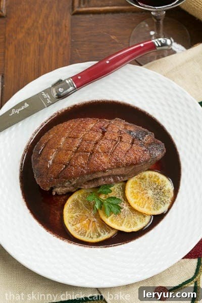 Gourmet Pan Seared Duck Breasts with Clementine Red Wine Sauce Pan Seared Duck Breasts with rich red wine sauce on a white plate, served with a red-handled knife.