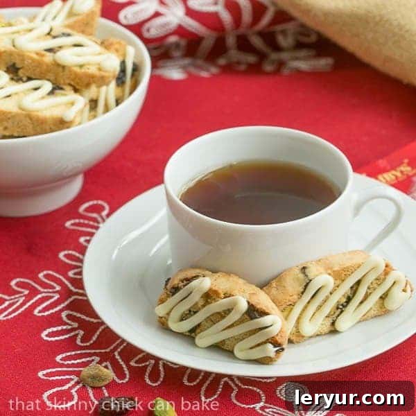 Cherry Pistachio Biscotti - Terrific holiday or hostess gift Two cherry pistachio biscotti arranged elegantly on a white saucer with a steaming cup of tea, inviting a moment of blissful indulgence.