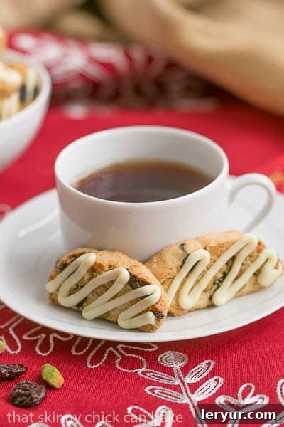 Cherry Pistachio Biscotti - Terrific holiday or hostess gift A close-up shot of Cherry Pistachio Biscotti resting on a white saucer, accompanied by a soothing cup of tea, ready to be enjoyed.