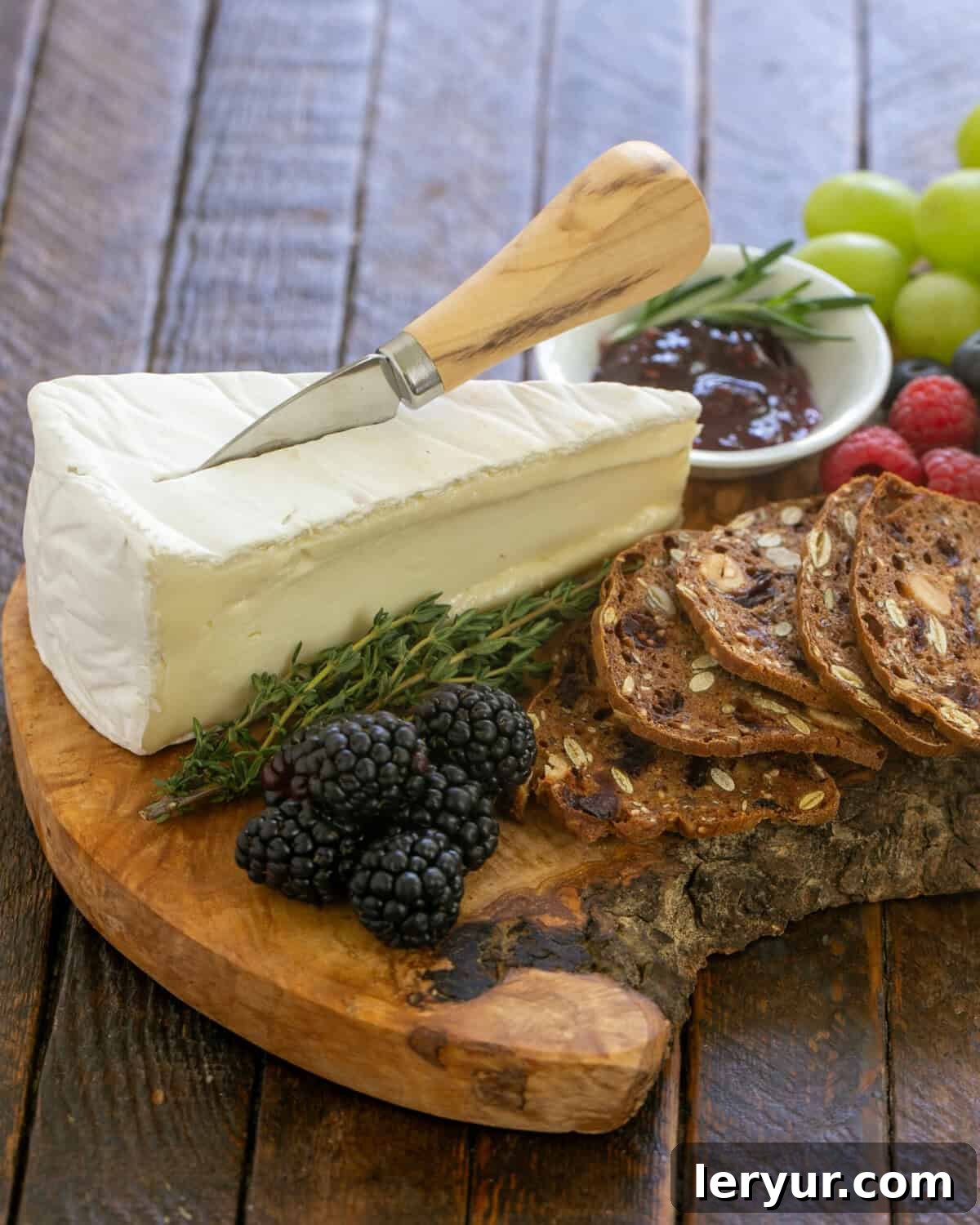 Brie with crackers and fruit on a beautiful wooden charcuterie board, ready for serving.