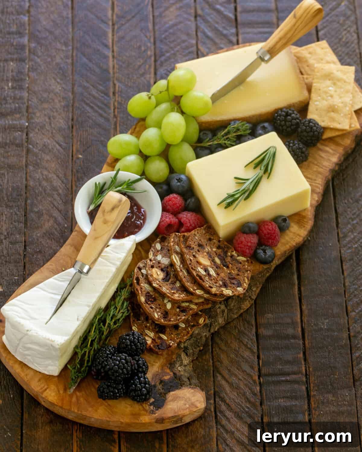 Overhead view of a wooden charcuterie board topped with an assortment of fruit, cheese, and crackers.