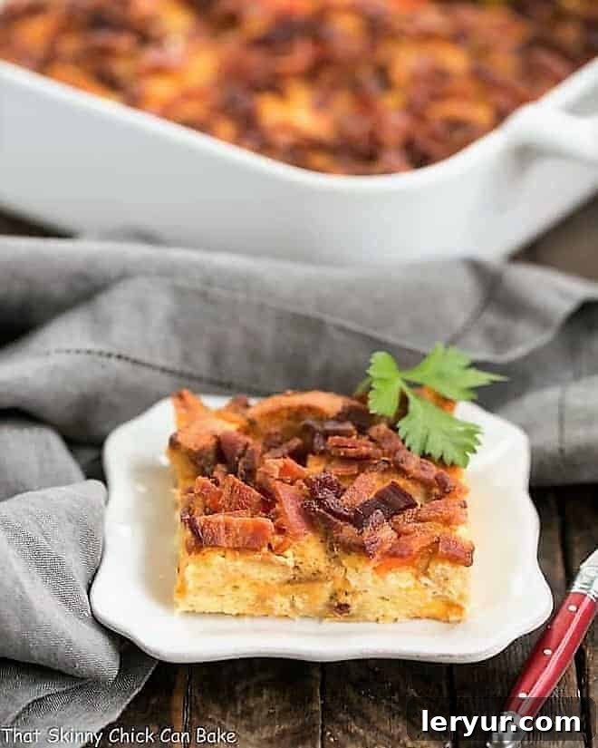Easy Bacon and Egg Strata - Golden brown breakfast casserole with croutons, cheese, bacon, and eggs A perfectly golden slice of Easy Bacon and Egg Strata, showcasing layers of crispy bacon, fluffy eggs, and melted cheese, served on a pristine white plate, with the full casserole dish blurred in the background.