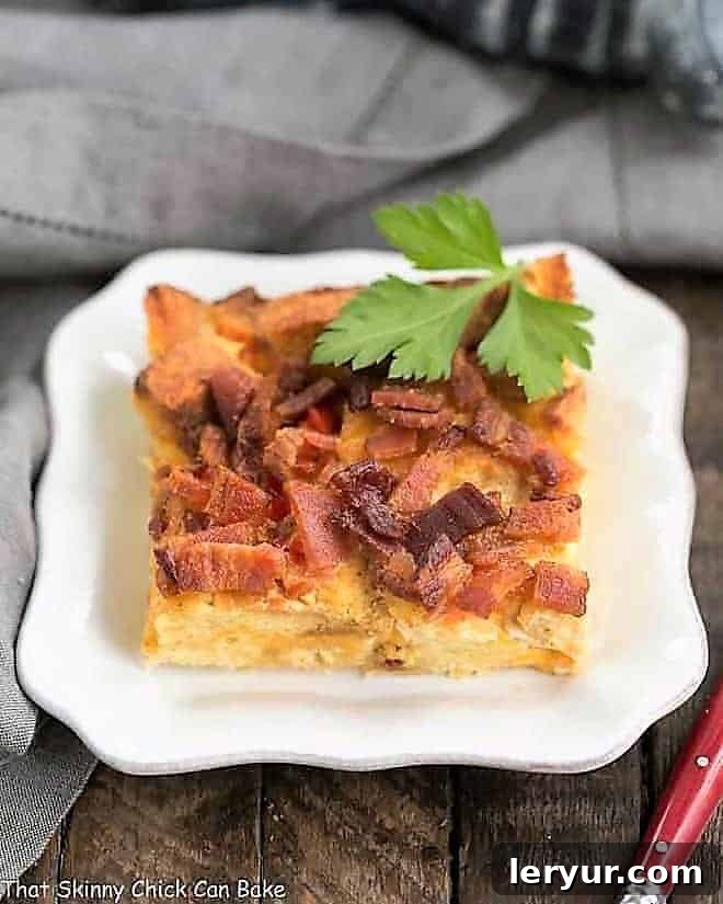 Easy Bacon and Egg Breakfast Casserole Recipe - Fluffy eggs, crispy bacon, savory croutons, and melted cheese A close-up shot of a single serving of Bacon and Egg Strata, perfectly baked with a golden crust, presented on a small white plate, ready to be enjoyed.