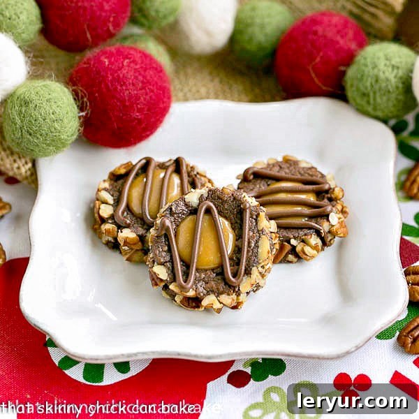 Close-up of three Turtle Thumbprint Cookies, showing the rich chocolate, caramel, and pecan toppings, on a white background.