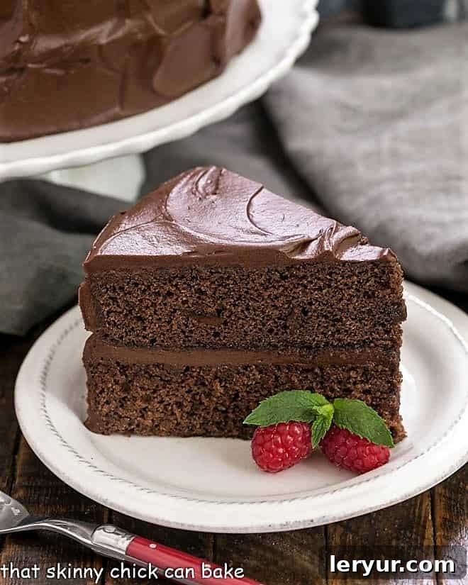 Best Chocolate Cake Recipe - rich, chocolaty and perfect for any celebration! Slice of Devil's Food Cake on a white dessert plate with a red handled fork with cake stand in the background.