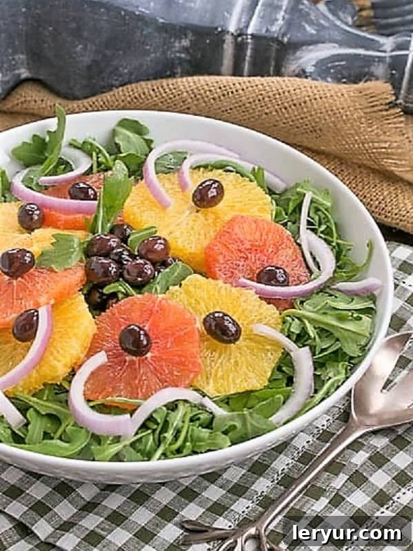 Vibrant Orange Olive Moroccan Salad presented on a bed of fresh arugula in a white bowl, resting on a charming checked napkin.