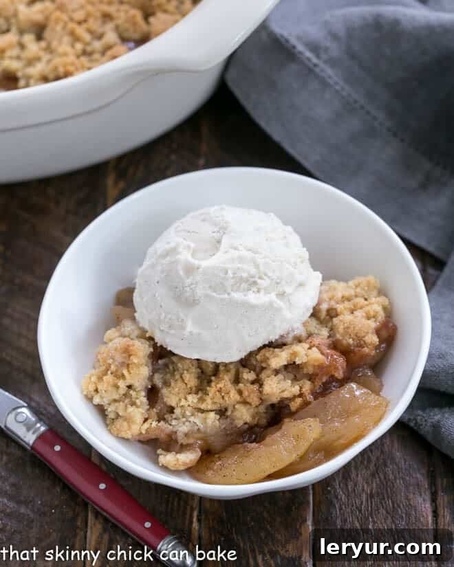Serving of Easy Apple Crisp in a small white bowl with a scoop of vanilla ice cream.