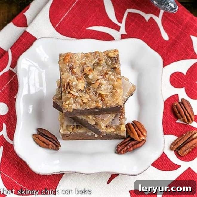 German Chocolate Brownies - Fudgy brownies topped with a caramelly, coconut, pecan topping Overhead view of a stack of German Chocolate Brownies on a square white plate with pecan halves. The golden-brown topping is visible, along with the dense brownie layers.