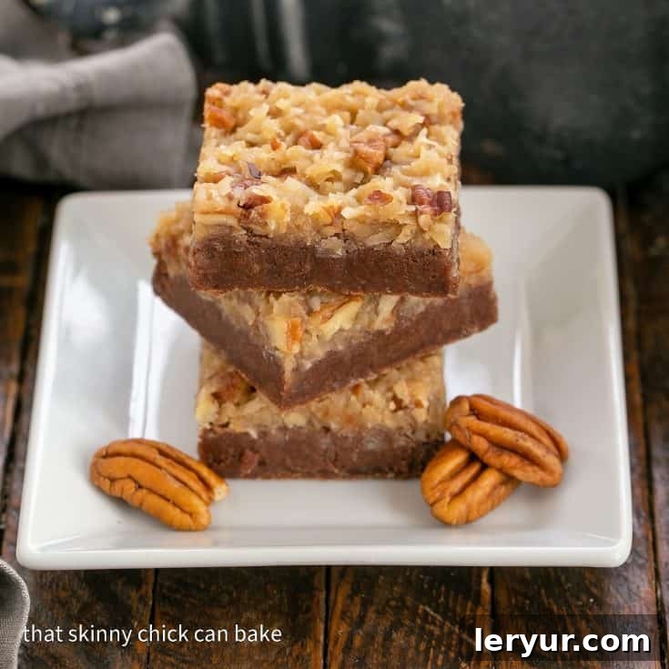 3 German chocolate brownies stacked on a square white plate with 3 pecans to garnish, highlighting the rich layers.