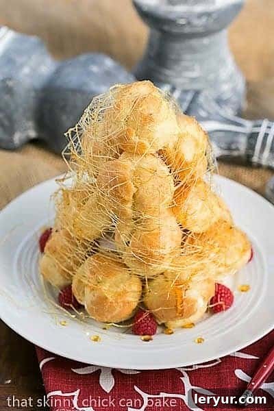 The stunning Lemon Cream Croquembouche, beautifully wrapped in a delicate web of spun sugar, presented on a elegant white serving plate. A vision of culinary art.
