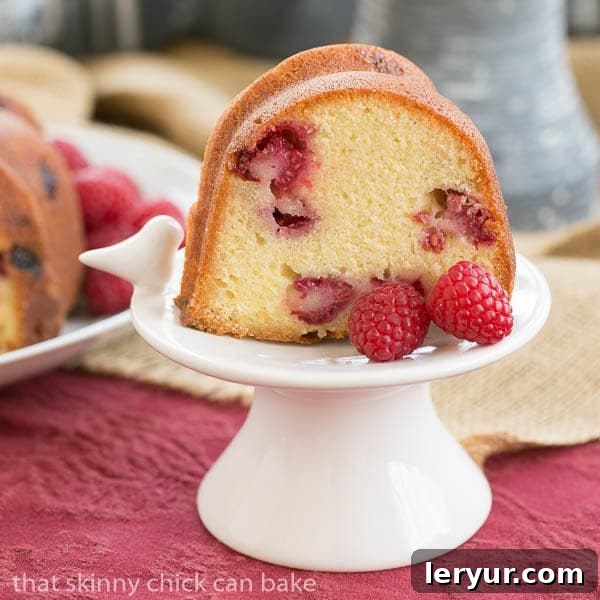 A perfectly sliced piece of Raspberry Amaretto Bundt Cake, revealing its dense crumb and pockets of fresh raspberries, served on a small white pedestal.