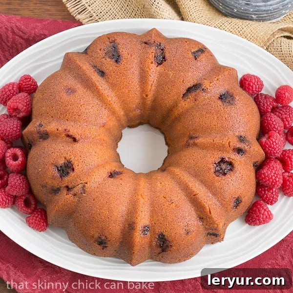 An inviting overhead view of the full Raspberry Amaretto Bundt Cake, showcasing its beautiful golden-brown crust and raspberry speckled interior, resting on a white, oval platter.