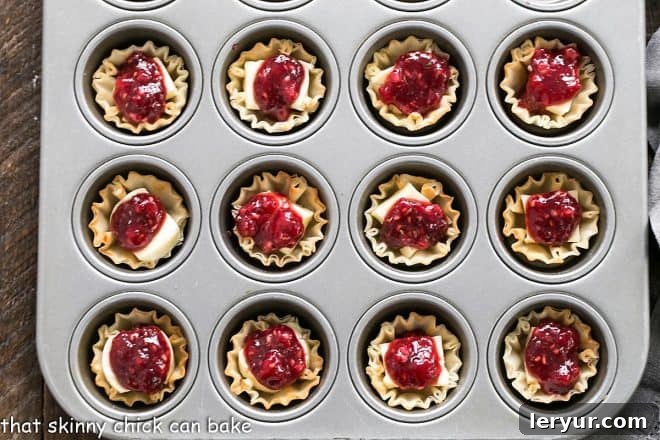 Unbaked Brie appetizers arranged in a mini muffin tin, ready for the oven.