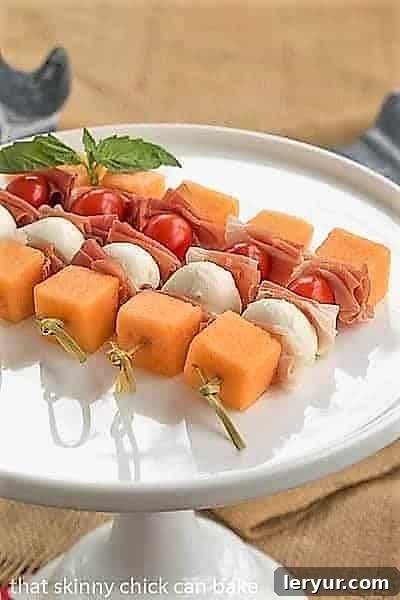 Refreshing Melon and Prosciutto Skewers with Basil Oil Melon and Prosciutto Skewers elegantly arranged on a white ceramic cake stand, showcasing the vibrant colors of the ingredients.