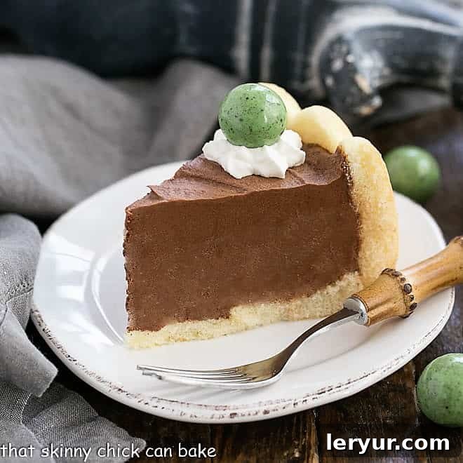 This Irish Chocolate Mousse Cake is infused with Irish Cream for a dreamy St. Patrick's Day Dessert! A perfectly portioned slice of Irish Chocolate Mousse Cake on a white ceramic plate, artfully garnished with a dollop of whipped cream and a festive green candy.