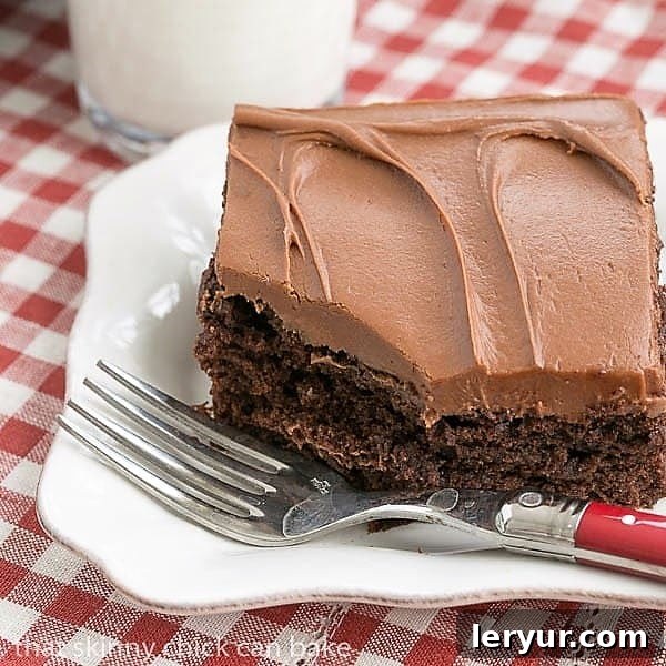 Cocoa Fudge Cake Recipe - Easy and outrageously delicious! A slice of Cocoa Fudge Cake on a pristine white plate, accompanied by a red-handled fork, inviting a delightful taste.