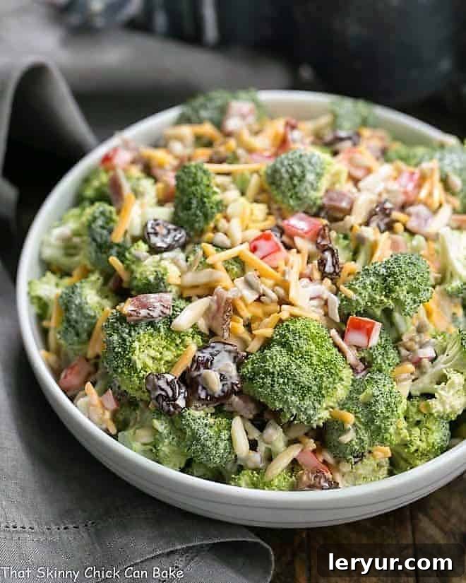 Broccoli Salad with Bacon and Dried Cherries - Perfect for picnics and potlucks! White ceramic bowl filled with Broccoli Salad with Bacon and Dried Cherries, garnished with fresh parsley.