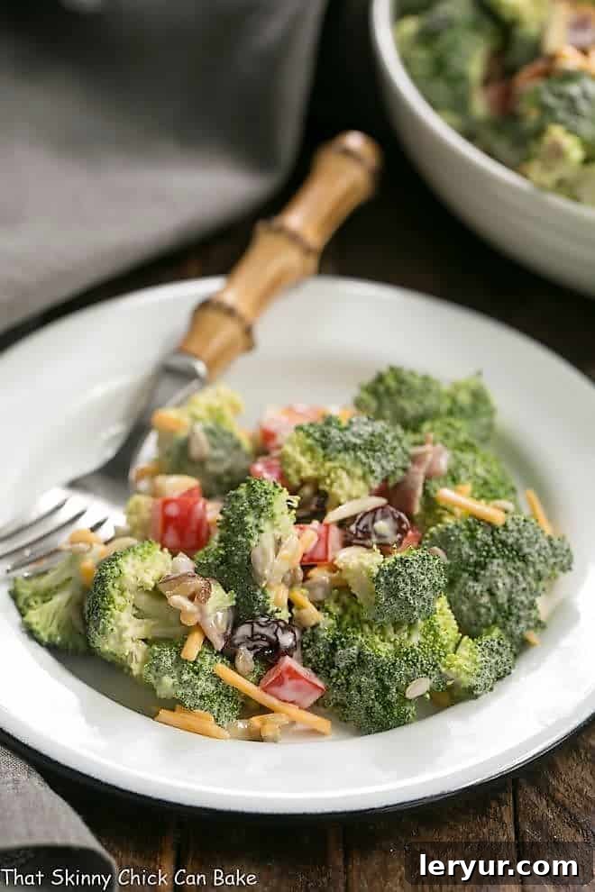 Broccoli Salad with Bacon and Dried Cherries - Perfect for picnics and potlucks! Broccoli Salad with Bacon and Dried Cherries on a white plate with a bamboo handled fork, ready to be eaten.