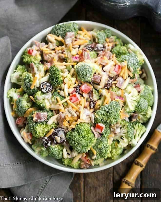 Broccoli Salad Recipe with Bacon and Dried Cherries - Perfect for picnics and potlucks! Overhead shot of Broccoli Salad with Bacon and Dried Cherries in a white serving bowl, garnished with fresh herbs.