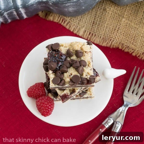 Chocolate Raspberry Crumb Bars - Shortbread, fudge, jam and a layer of crumbs makes for an out of this world bar cookie! Overhead view of Chocolate Raspberry Crumb Bars arranged on a white pedestal, resting on a vibrant red napkin, highlighting the rich colors and textures.
