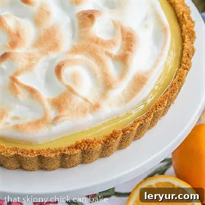 Close-up view of a slice of Meyer Lemon Tart with Meringue Topping on a white cake stand, showing the layers of crust, filling, and meringue.