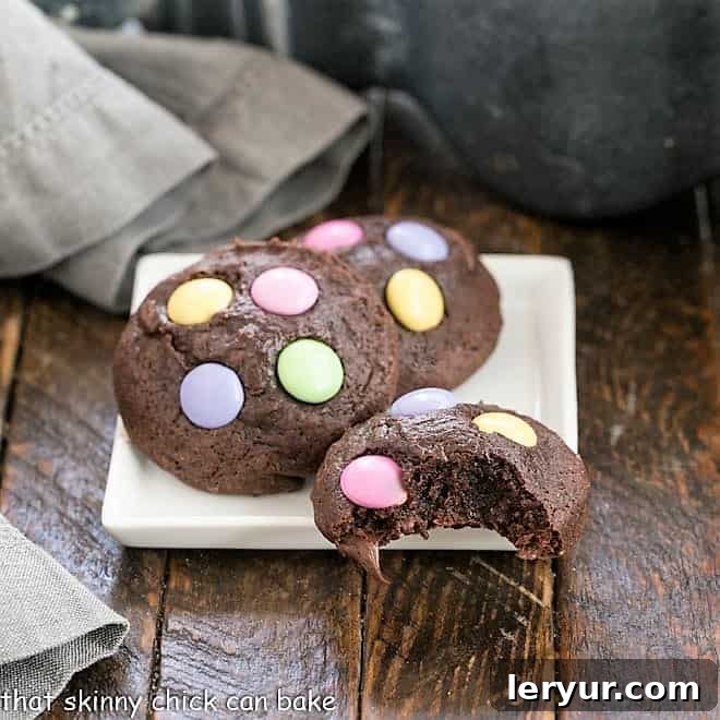 Three perfectly baked Brownie Cookies presented on a square white plate, with one cookie having a bite taken out, revealing its fudgy interior and chocolate chips.